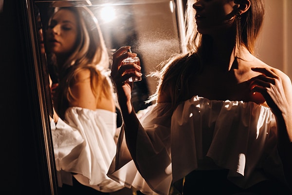 Eine Frau parfümiert sich im Abendkleid vor einem Spiegel
