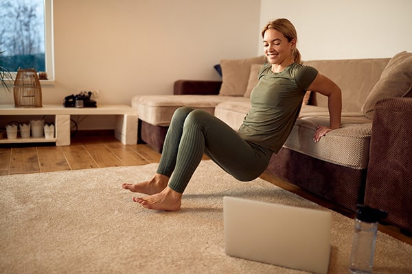 Eine fröhliche Frau trainiert Trizeps Dips an ihrem Sofa